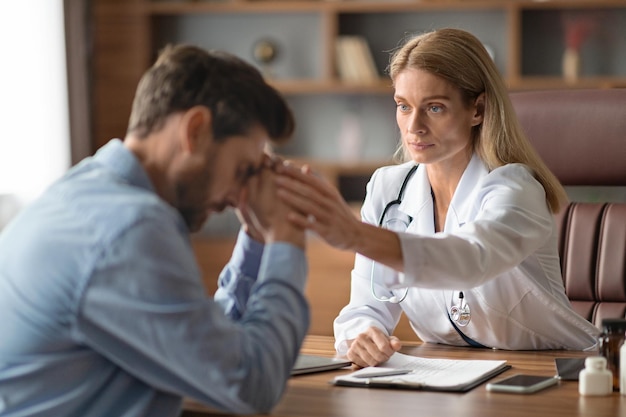 Doctor mujer reconfortante molesto paciente masculino durante la reunión en la clínica