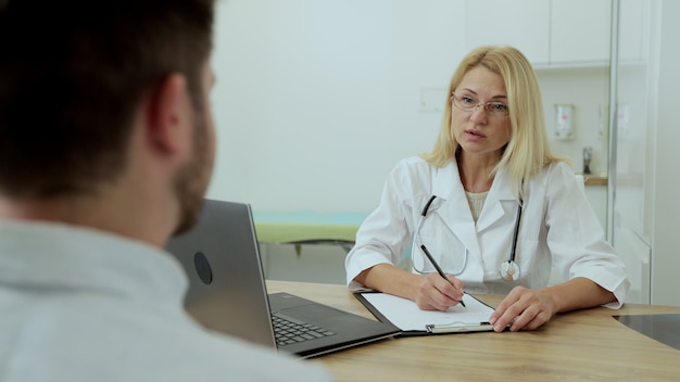 Doctor mujer sentada en el consultorio médico hablando con el paciente durante la consulta. Concepto de servicio de atención médica, médico y personal médico.