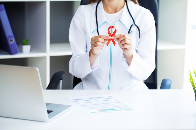 Doctor mujer sosteniendo una cinta roja emerge de una situación crítica después de superar el SIDA