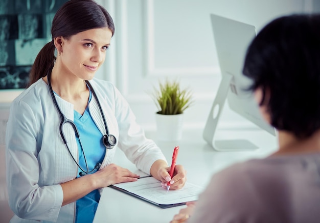 Doctor y paciente discutiendo problemas médicos en una sala de consulta del hospital Doc llenando el formulario de un paciente