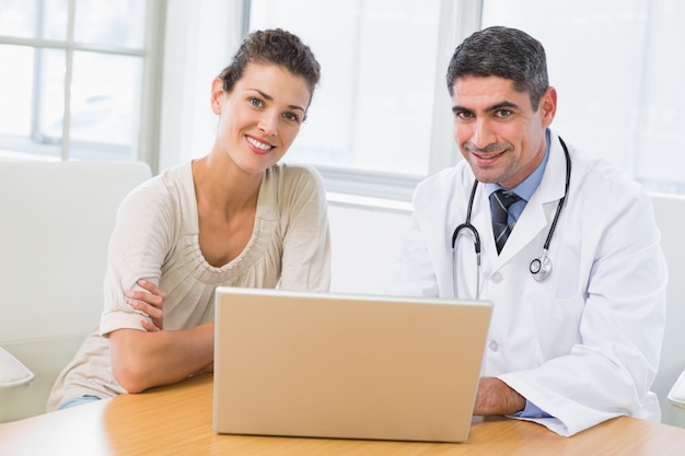 Doctor y paciente que usa la computadora portátil en la oficina médica
