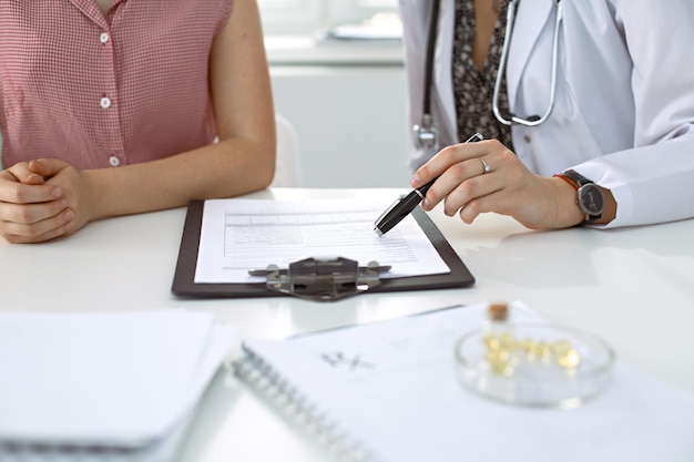 Doctor y paciente sentados en el escritorio. Médico señalando registros de historial médico y explicando algo a una mujer joven. Concepto de medicina y atención de la salud.