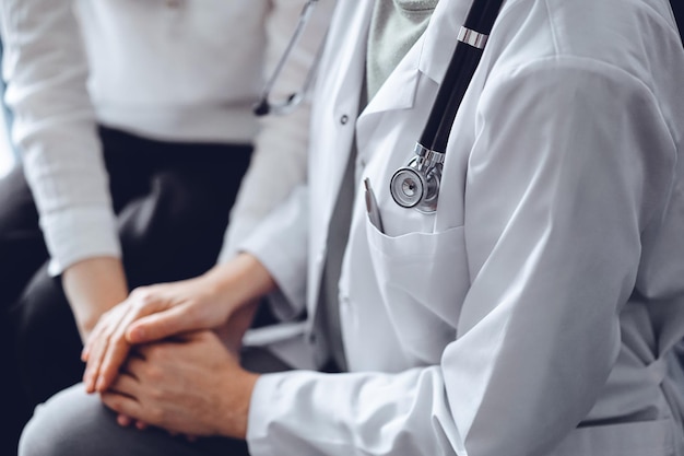 Doctor y paciente sentados en el sofá. La atención se centra en las manos de una médica que tranquiliza a la mujer, de cerca. Concepto de medicina.