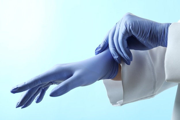 Doctor poniendo guantes médicos sobre fondo azul aislado