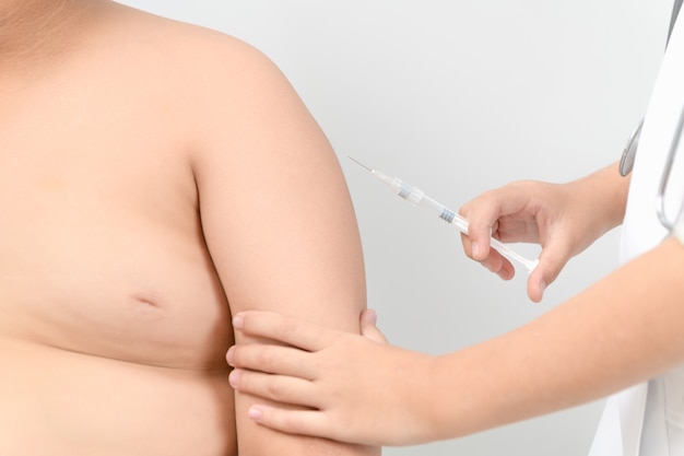 El doctor prepara la vacuna inyectable en el brazo del niño gordo obeso