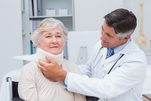 Doctor que examina al paciente mayor que usa el apoyo del cuello