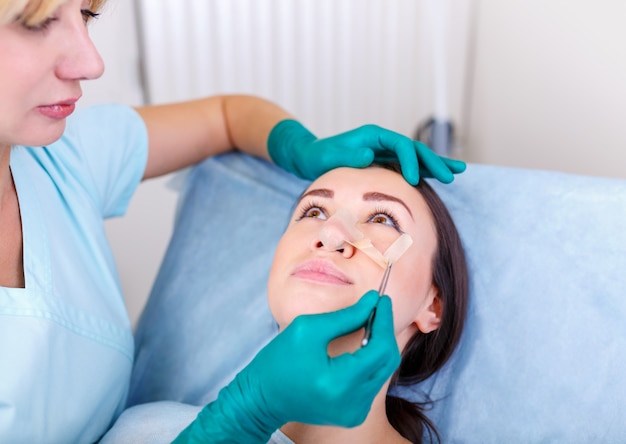 Doctor revisando la cara de la mujer, el njse después de una cirugía plástica, rinoplastia, blefaroplastia.