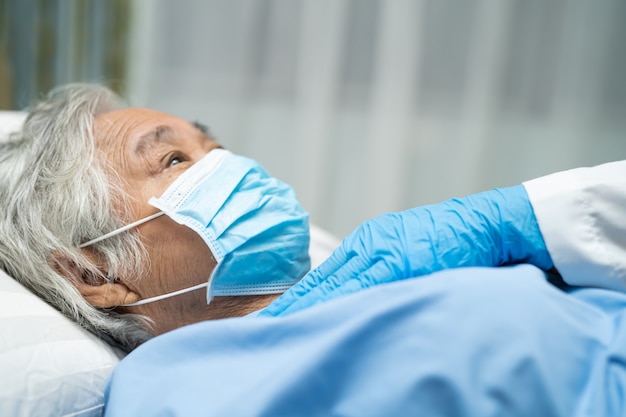 Doctor revisando a una paciente asiática mayor que usa una mascarilla en el hospital para proteger el coronavirus Covid-19.