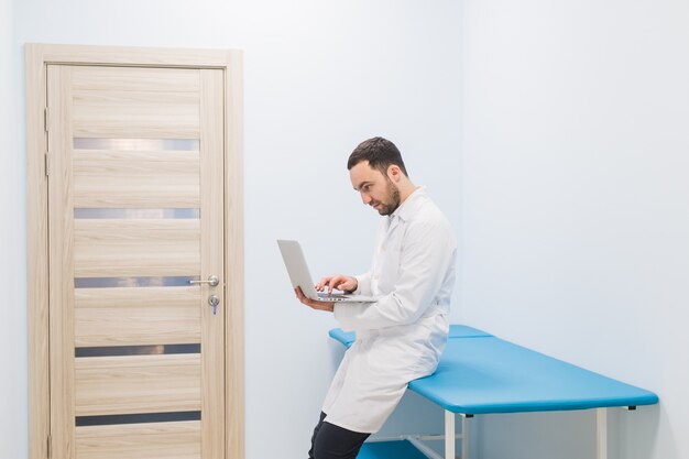 Doctor sentado en una cama de hospital con su computadora portátil