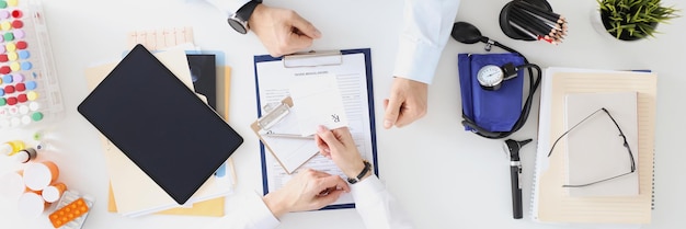 Doctor sentado a la mesa y escribiendo una receta para el concepto de atención médica de la vista superior del paciente