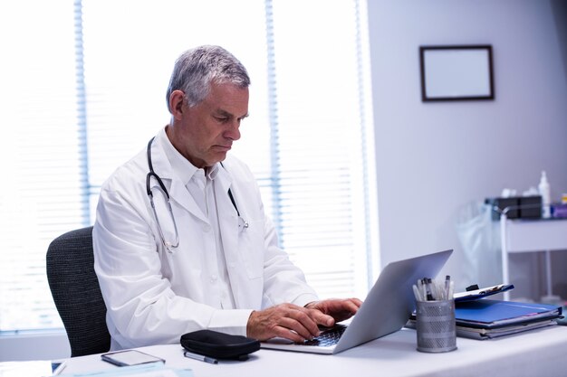 Doctor sentado en la mesa y usando laptop