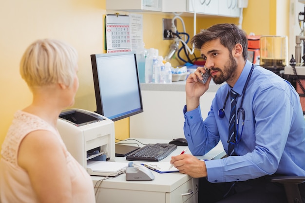 Foto doctor sentado en su escritorio y hablando por teléfono