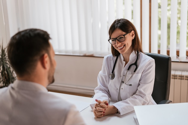 Doctor de sexo femenino feliz que discute con el paciente en la tabla en clínica