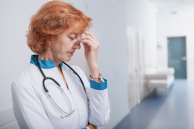 Doctor de sexo femenino mayor que parece cansado después de día laborable largo en el hospital.