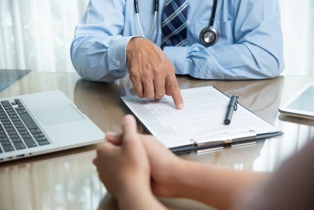 Doctor de sexo masculino mayor en camisa azul que discute con su paciente.