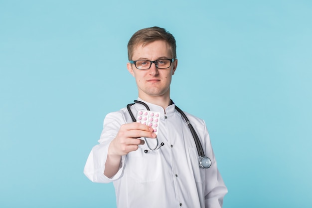 Doctor de sexo masculino que muestra pastillas de color rosa. Médico joven sosteniendo medicamentos sobre fondo azul.