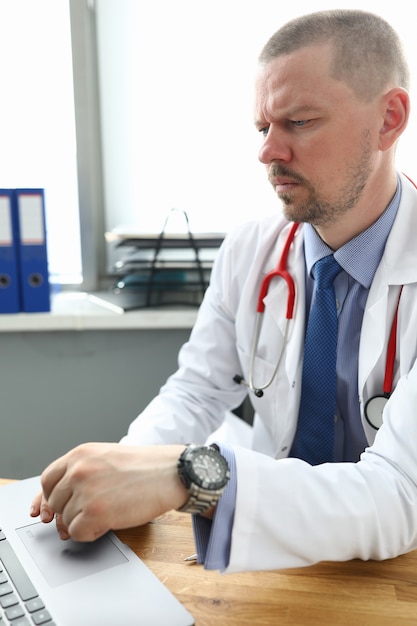 El doctor sienta la mesa en la oficina y trabaja con la computadora portátil