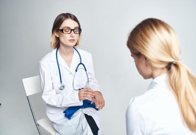 El doctor se sienta en una silla y una paciente en el interior sobre un fondo claro