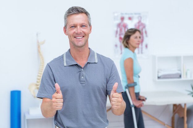 Doctor sonriendo a la cámara mientras su paciente de pie con muleta