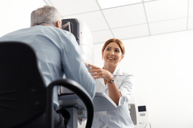 Doctor sonriendo. Hermosa joven médico con bata de laboratorio blanca sonriendo mientras examina al hombre jubilado