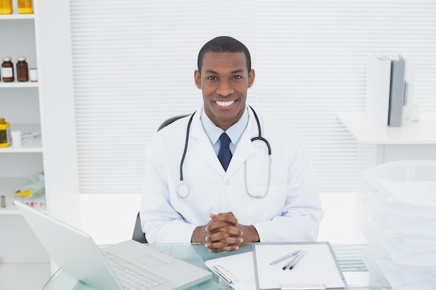 Doctor sonriente con la computadora portátil en la oficina médica
