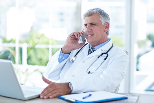 Doctor sonriente con llamada telefónica en su escritorio