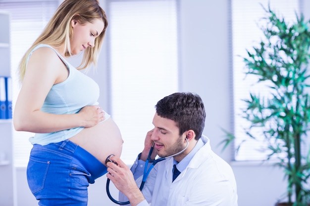 Doctor sonriente que examina el estómago del paciente embarazada de pie