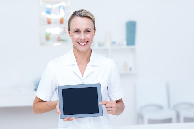 Doctor sonriente que mira la cámara y que muestra la tableta