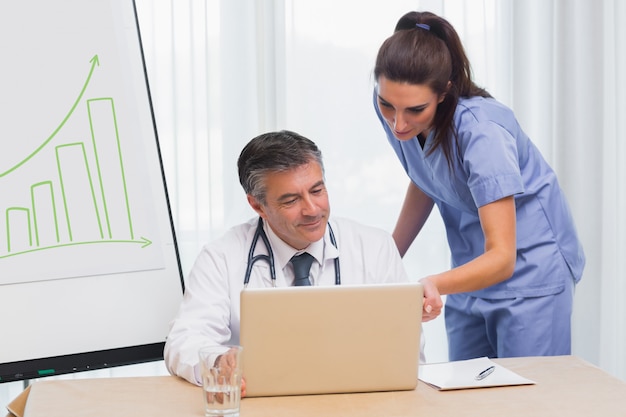 Doctor sonriente que muestra a enfermera algo en la computadora portátil