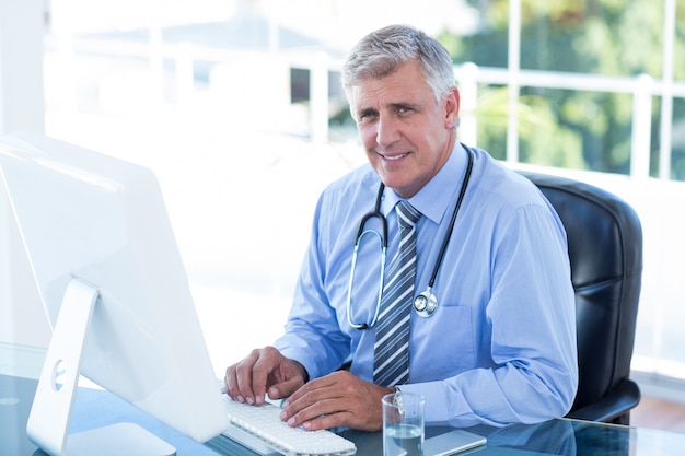 Doctor sonriente que trabaja en la computadora en su escritorio