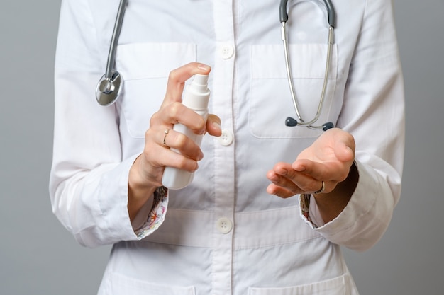 Doctor sosteniendo una botella de spray de alcohol. El médico recomienda usar gel antiséptico. Aislado en gris