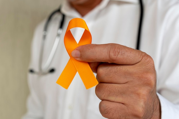 Doctor sosteniendo una cinta naranja. campaña para prevenir el cáncer de piel, melanoma, diciembre naranja