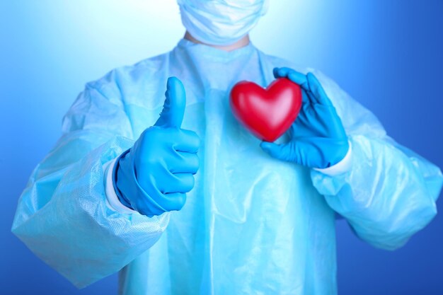 Doctor sosteniendo corazón decorativo sobre fondo azul.