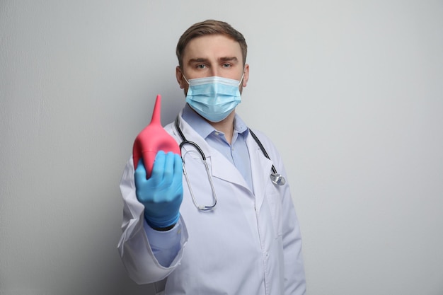 Doctor sosteniendo enema de goma sobre fondo gris