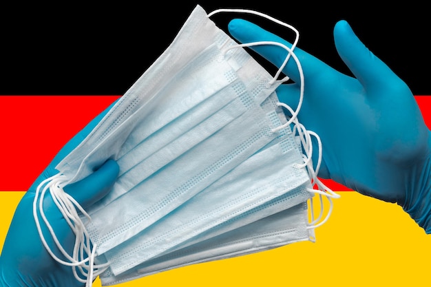 Doctor sosteniendo mascarillas médicas en manos guantes azules sobre fondo bandera nacional de alemania concepto ...