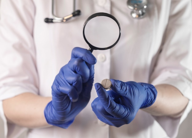 Doctor sosteniendo la píldora en los dedos primer plano de la mano femenina con la medicina y la lupa en la mano en el globo ...