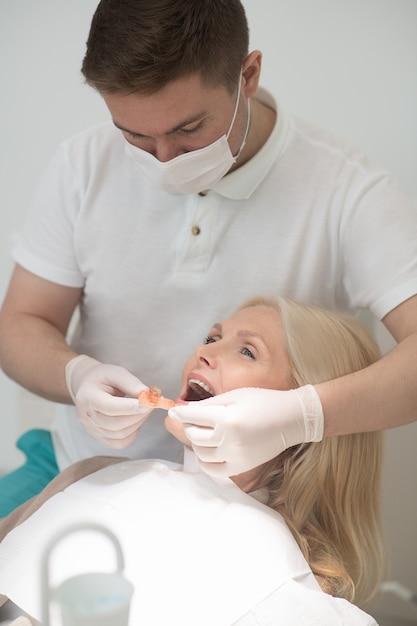 Doctor sosteniendo una prótesis dental y preparándose para ponerla en la boca del paciente