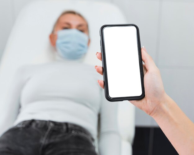 Foto doctor sosteniendo un teléfono en blanco junto al paciente borroso