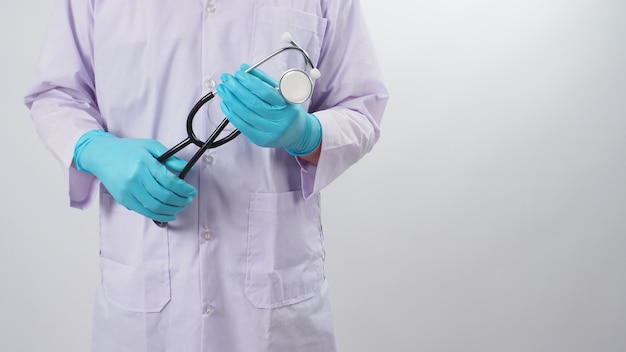 El doctor sostiene el estetoscopio en la mano con guantes de látex azul sobre fondo blanco.