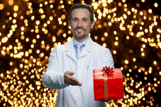 El doctor te da un regalo para Navidad. Apuntando a la caja de regalo roja. Muchas luces brillantes en el fondo.