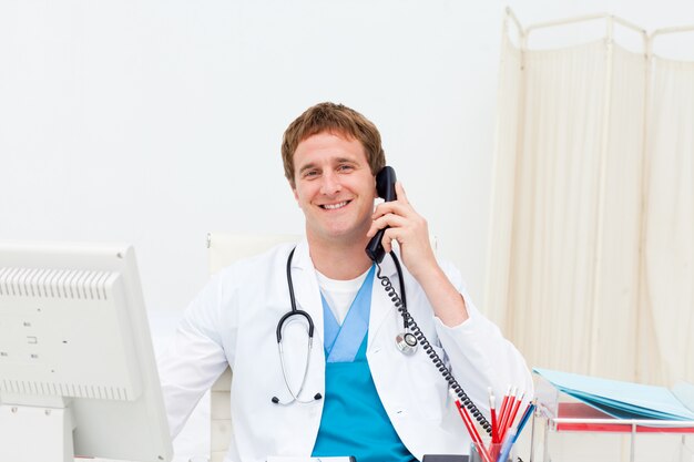 Un doctor en el teléfono sonriendo a la cámara.