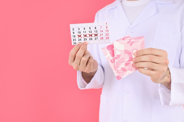 Doctor tiene calendario menstrual y almohadillas sobre fondo rosa