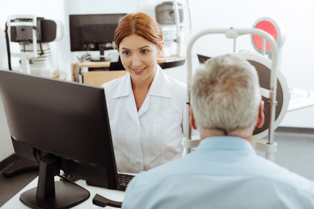 Doctor trabajando duro. Oftalmólogo joven pero profesional pelirrojo trabajando duro mientras examina al paciente