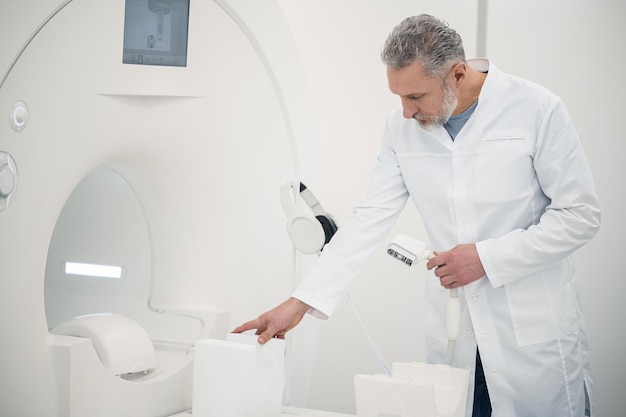 Doctor en el trabajo Doctor en una bata de laboratorio de pie cerca de un escáner de resonancia magnética