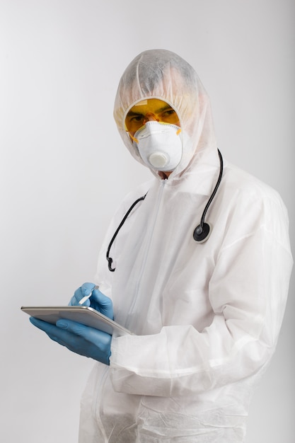 Doctor en traje antidémico tomando notas en tableta electrónica personal