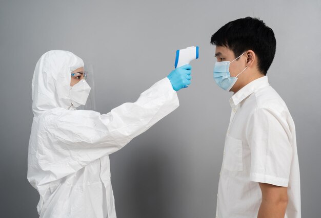 Doctor en traje de protección PPE usando termómetro infrarrojo midiendo la temperatura con personas, IR Thermoscan