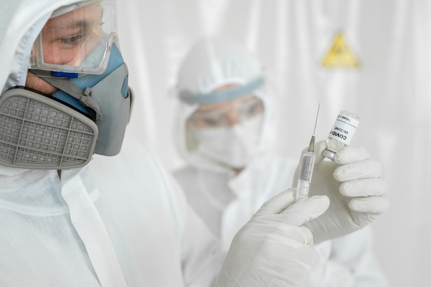 Doctor con traje protector y máscara sostiene una jeringa de inyección y vacuna COVID-19. Científicos de laboratorio en un mono realizando una investigación sobre una vacuna.
