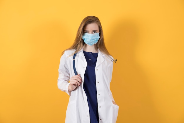 Doctor en traje quirúrgico, bata blanca y mascarilla médica sobre un fondo amarillo