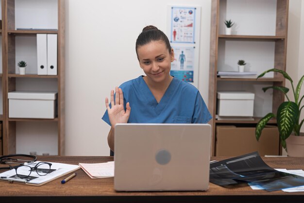 Foto doctor en uniforme azul dando la bienvenida al paciente en su computadora portátil durante una consulta en línea