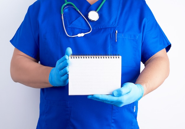 Doctor en uniforme azul y guantes de látex estériles con cuaderno abierto en blanco